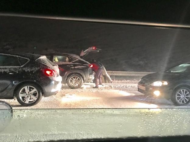 Dos personas buscan en el interior de su vehículo, apartado en un arcén de la autopista de peaje en plena noche, con la carretera llena de nieve. 
