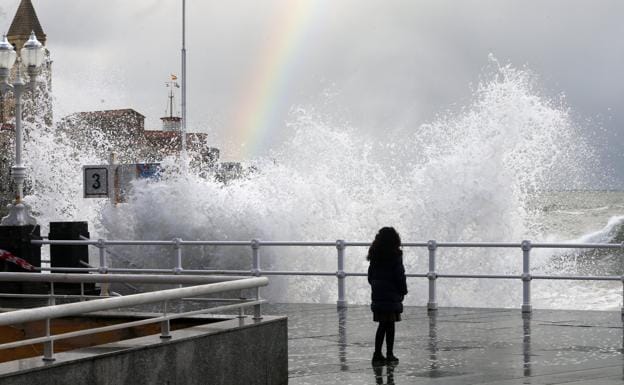 Imagen. Una joven contempla el fuerte oleaje desde el paseo del Muro, con el arcoíris sobre la bahía.