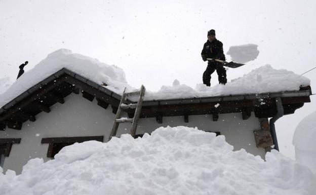 Imagen. Un hombre retira la nieve del tejado de su casa en Pajares.