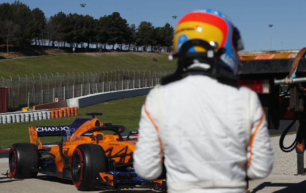 Fernando Alonso, de espaldas, observa como retiran su coche de la pista. 