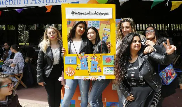 Varias jóvenes posan en el Pueblo de Asturias junto a un cartel contra la segregación escolar. 