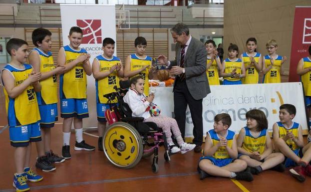 Shamira Alonso recibe un pequeño trofeo entregado por López Ferrer, acompañados por un grupo de jóvenes participantes en las actividades de la Fundación Gijón Baloncesto. 