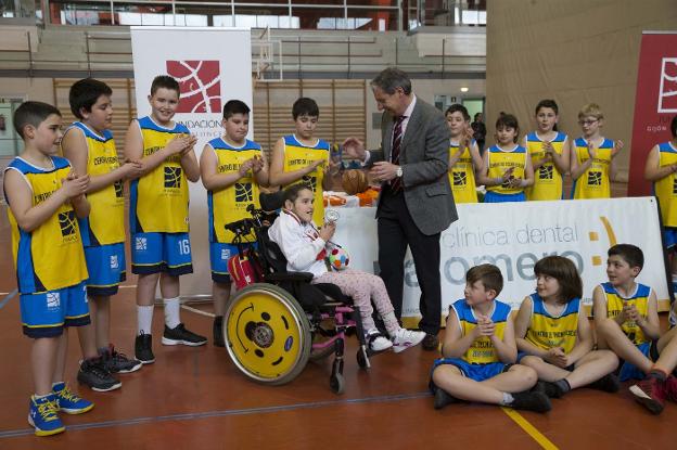 Shamira Alonso recibe un pequeño trofeo de manos de López Ferrer, acompañados por un grupo de jóvenes participantes en las actividades de la Fundación Gijón Baloncesto. 