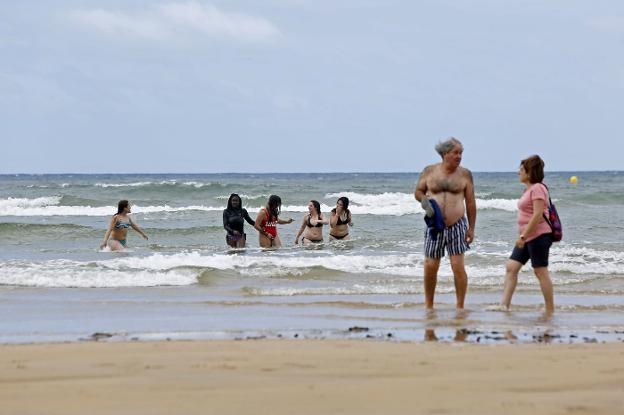 Un grupo de jóvenes se baña en la playa de San Lorenzo, ayer, mientras una pareja conversa en la orilla. 