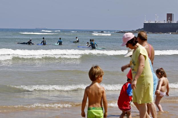 Un grupo de bañistas, en la playa de San Lorenzo, con varios surfistas al fondo. 