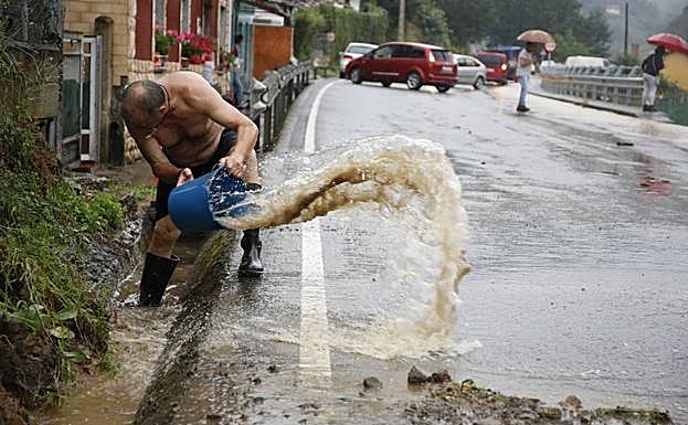 Un vecino achica agua de una cuneta en la carretera de Santo Emiliano, cortada por la lluvia y un argayo.