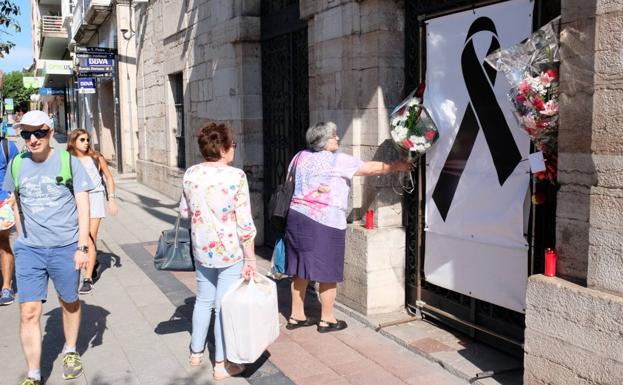 Una vecina coloca un ramo de flores junto al lazo negro colgado en el Consistorio llanisco en memoria de Ardines. 