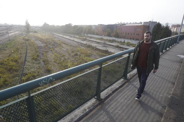 Adrián Arias pasea sobre el puente de Carlos Marx. Al fondo, los terrenos del 'solarón' que esperan a ser adecentados. 