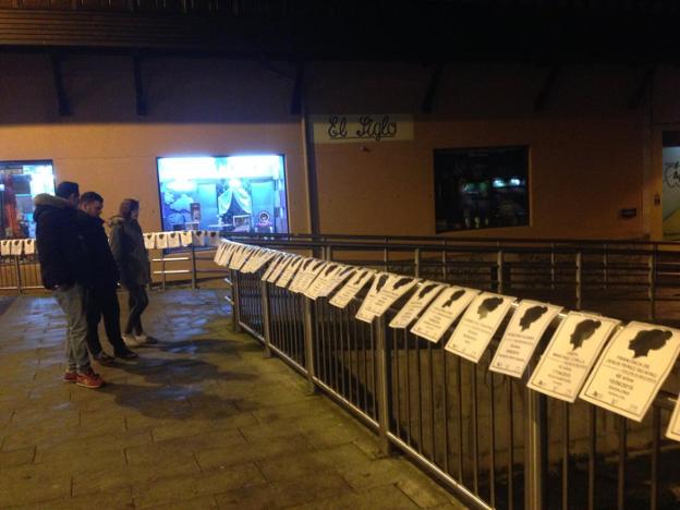 Varias personas contemplan las esquelas colocadas en el puente de Llanes. 