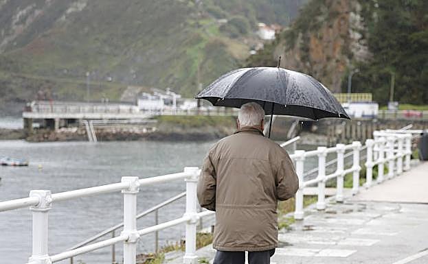 Un hombre pasea bajo la lluvia en Cudillero.