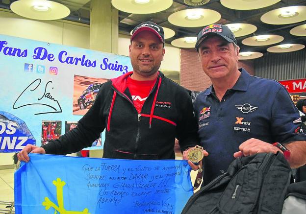 Javier Álvarez, con la bandera de Asturias con la que recorrió el Dakar y su medalla de 'finisher', y Carlos Sainz, a su llegada ayer al aeropuerto de Barajas tras un maratoniano viaje de regreso.