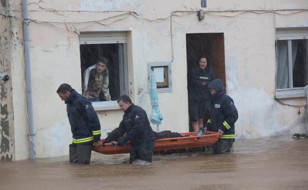 Los bomberos sacan a una mujer mayor de una casa ya inundada en Raíces, Castrillón. :: MARIETA