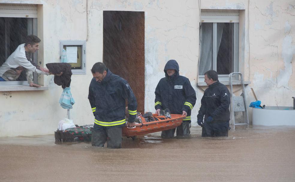 Un equipo de bomberos rescata a una anciana de una vivienda inundada en Castrillón. 