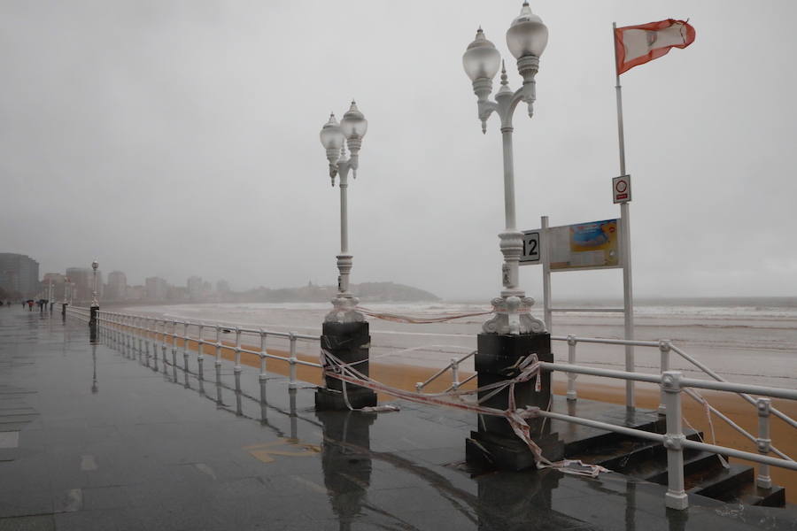 El paseo gijonés del Muro ha amanecido con algunas de sus escaleras cerradas debido a los daños causados por el temporal de lluvia y viento. Operarios de Emulsa han procedido a la limpieza de la arena depositada en el paseo tras la pleamar.