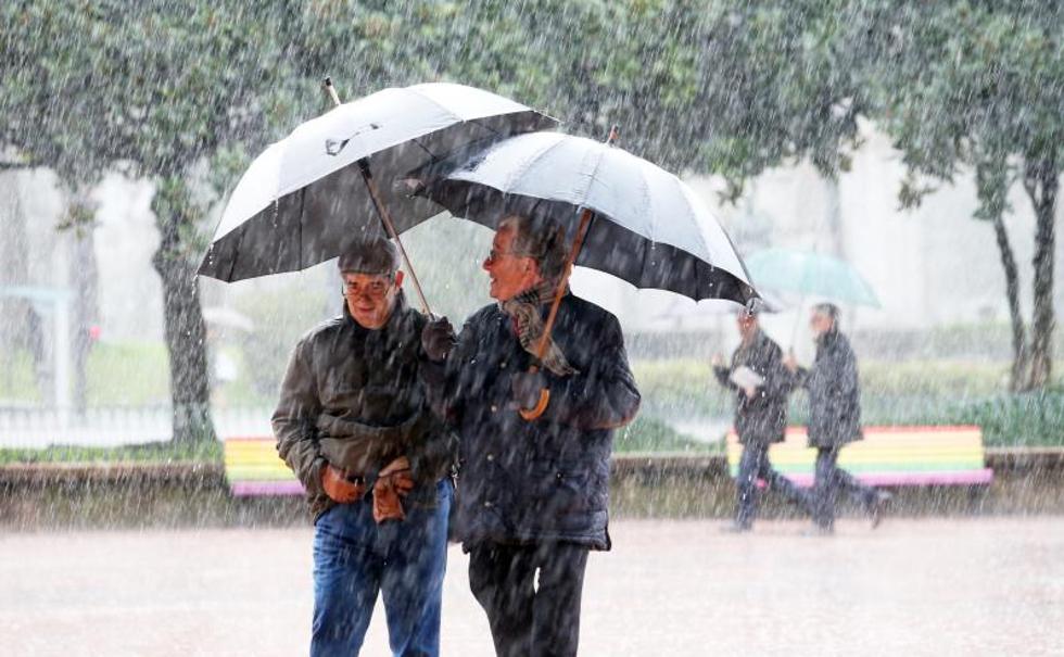 Dos hombres se protegen de la intensa lluvia, esta mañana, en Oviedo.
