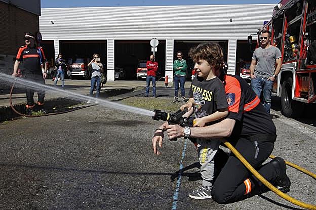 Un niño activa la manguera con la ayuda de un bombero, en el parque de Roces. 