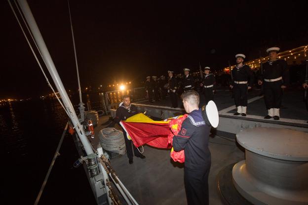 Dos marineros terminan de recoger la bandera de España delante de la guardia militar de la fragata. 