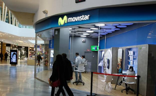 Una pareja pasa junto a una tienda de Movistar en un centro comercial.