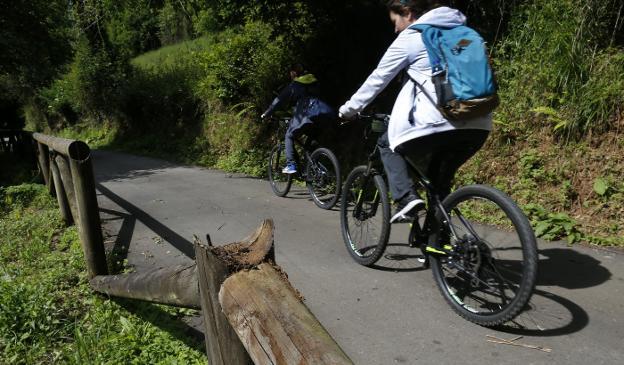 Dos ciclistas pasan junto a una de las numerosas vallas rotas de la Senda del Oso. 