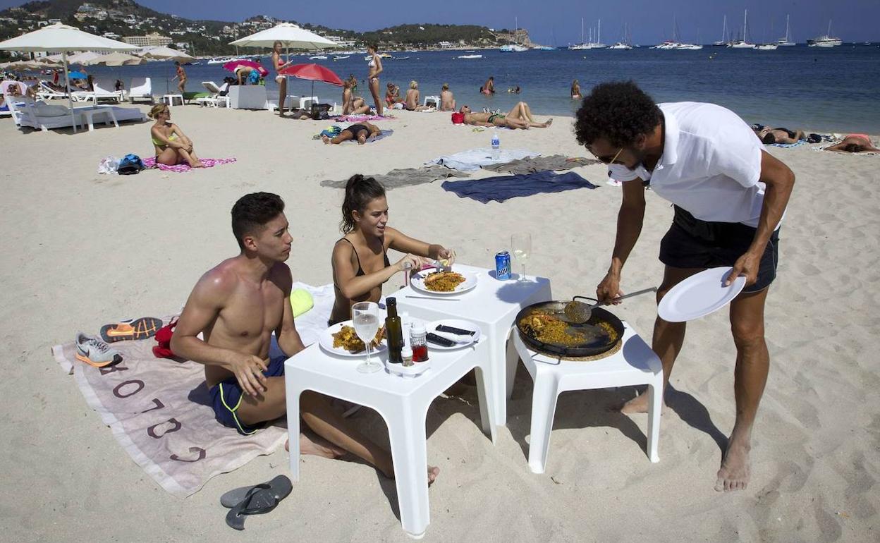 Un camarero sirve una paella a los clientes en la playa de Talamanca. 