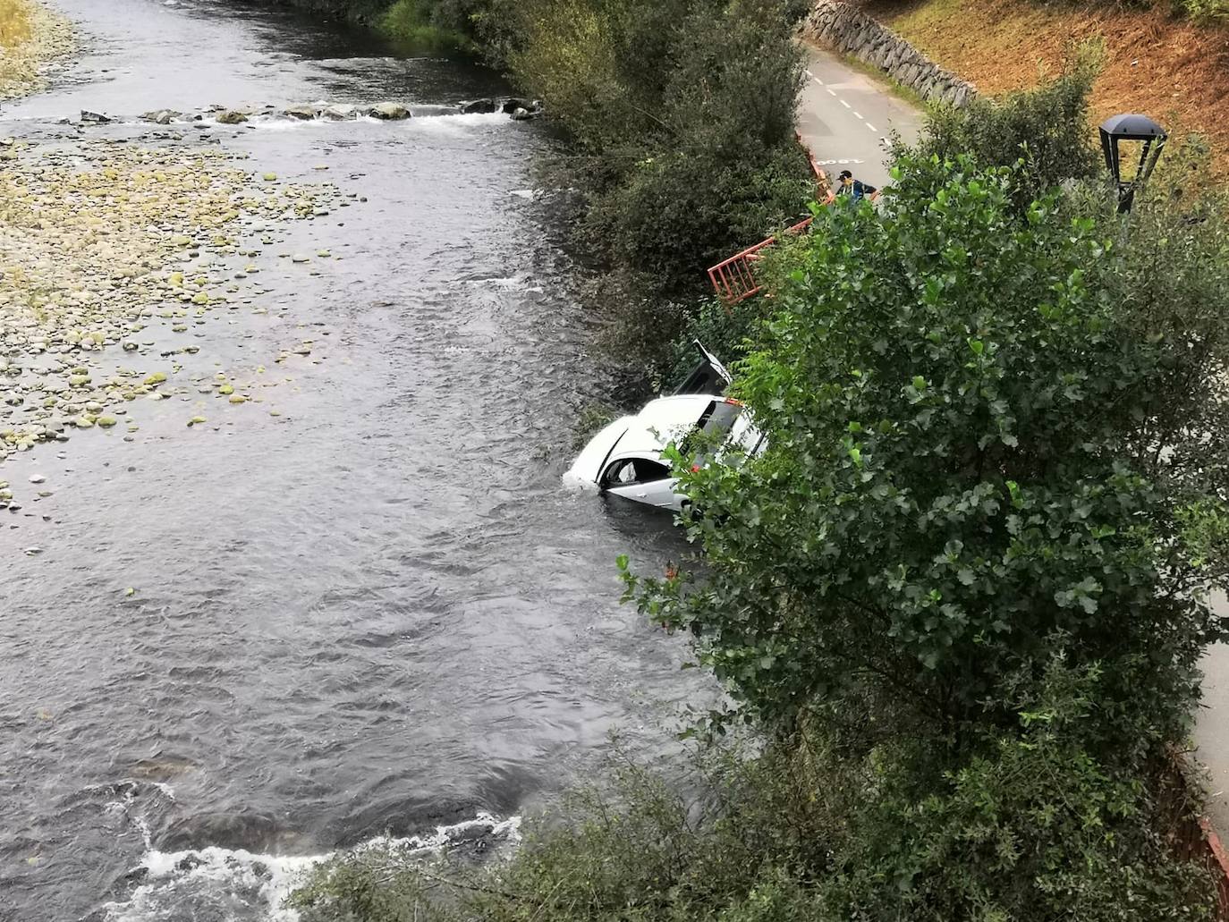Espectacular accidente con un herido leve. Un coche con cuatro ocupantes que circulaba por la carretera AS-117 ha caído al río Nalón en El Entrego. El conductor triplicaba la tasa de alcoholemia.