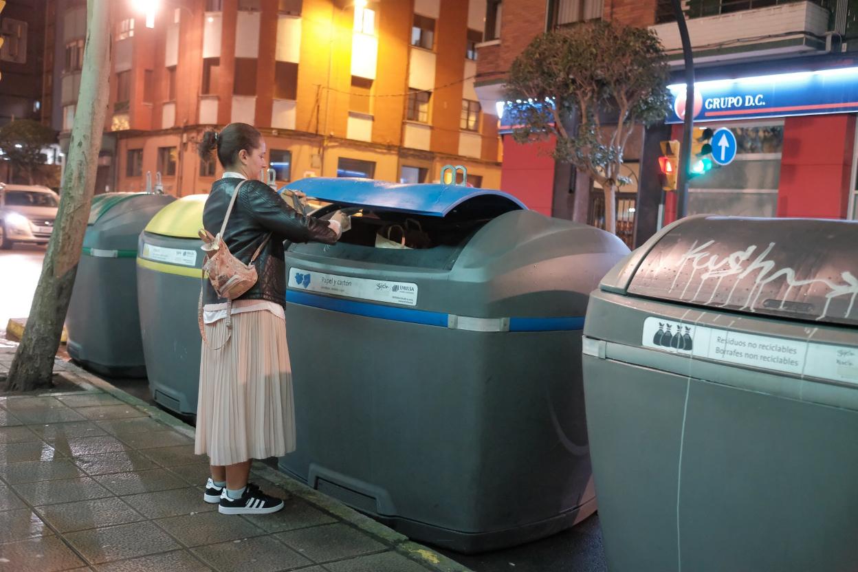 Una mujer tira basura en el contenedor de papel. 