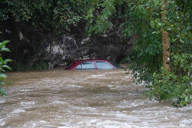 Un vehículo, atrapado por la riada en la localidad de Debodes, en Llanes, donde se produjeron abundantes daños y varios pueblos quedaron aislados.