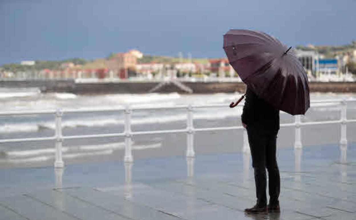 Un viandante, se protege de la lluvia con su paraguas en Gijón. 