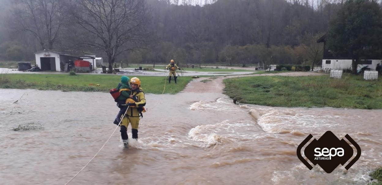 Los bomberos sacan a un niño en brazos tras inundarse el acceso a su casa en La Reboria, en el concejo de Piloña. 