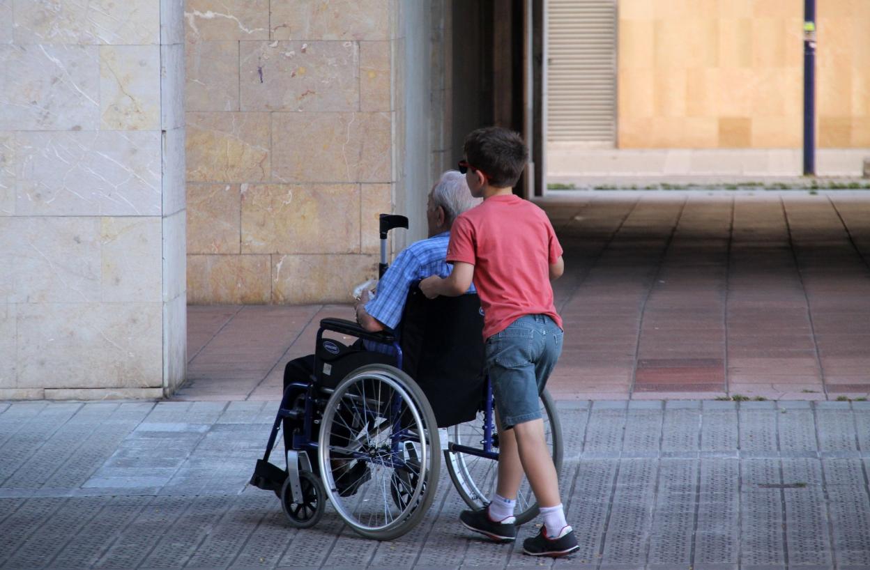 Un niño ayuda a su abuelo, en una silla de ruedas. 