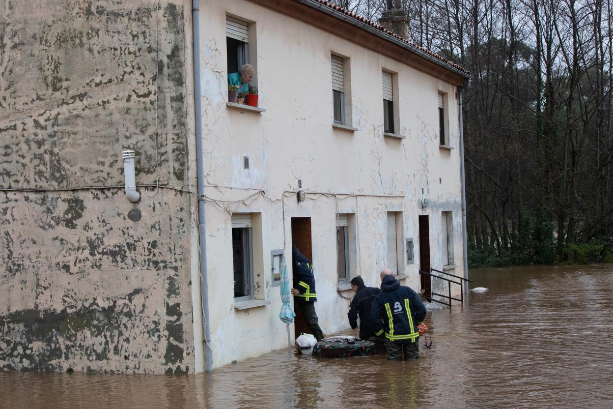 Los bomberos ayudan a abandonar su domicilio a una familia tras el desbordamiento del río Raíces. 