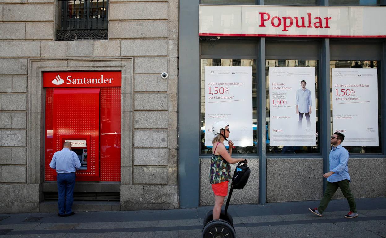 Un hombre saca dinero de un cajero del Santander al lado de una sucursal del Popular, en Madrid