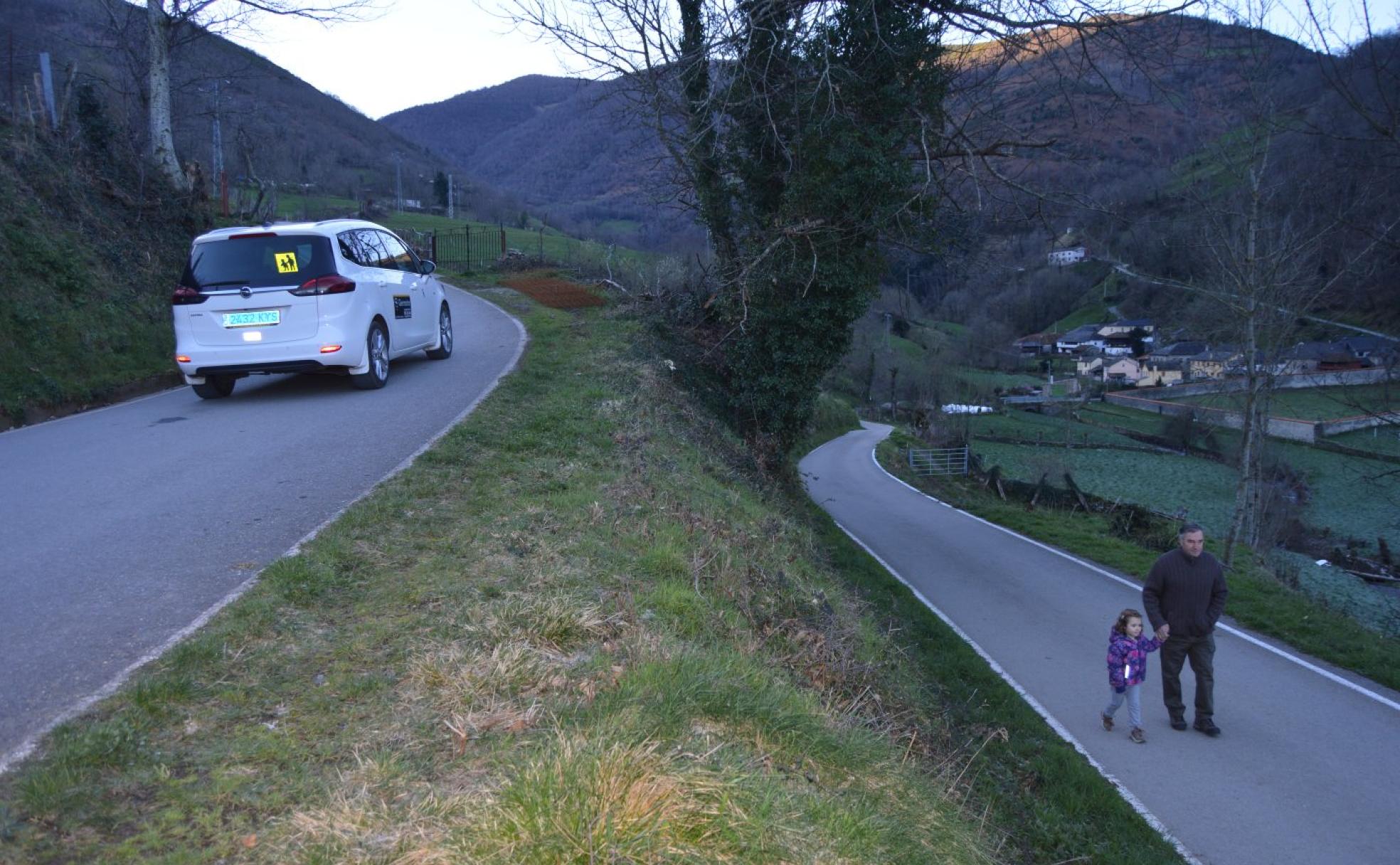 María López y su abuelo Bernardo caminan por la carretera que recorren a diario para llegar al colegio, tras haberles adelantado el taxi que hace la ruta escolar hasta Llamera.