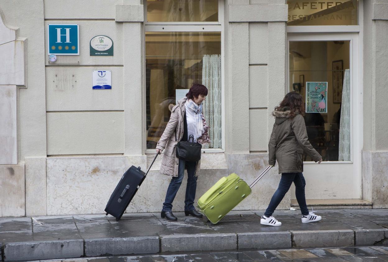 Una turista abandona un hotel en Gijón con su equipaje. 