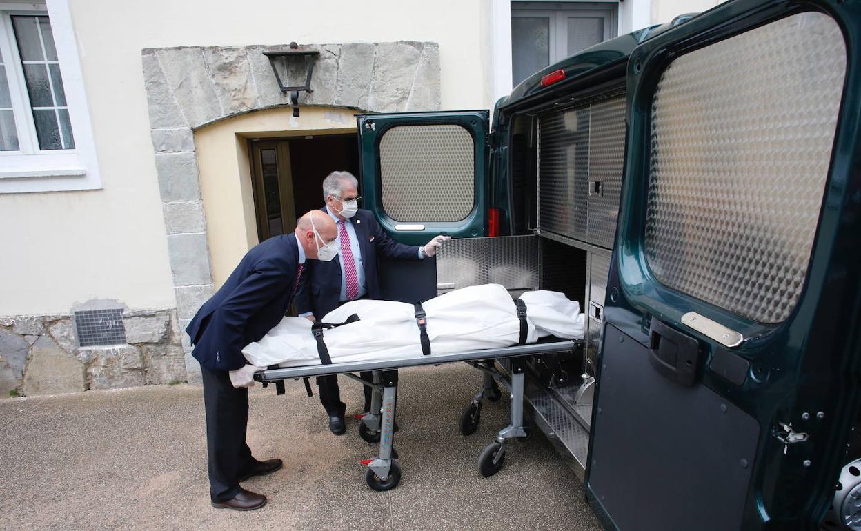 Los trabajadores de la funeraría introducen el cadáver en el vehículo.