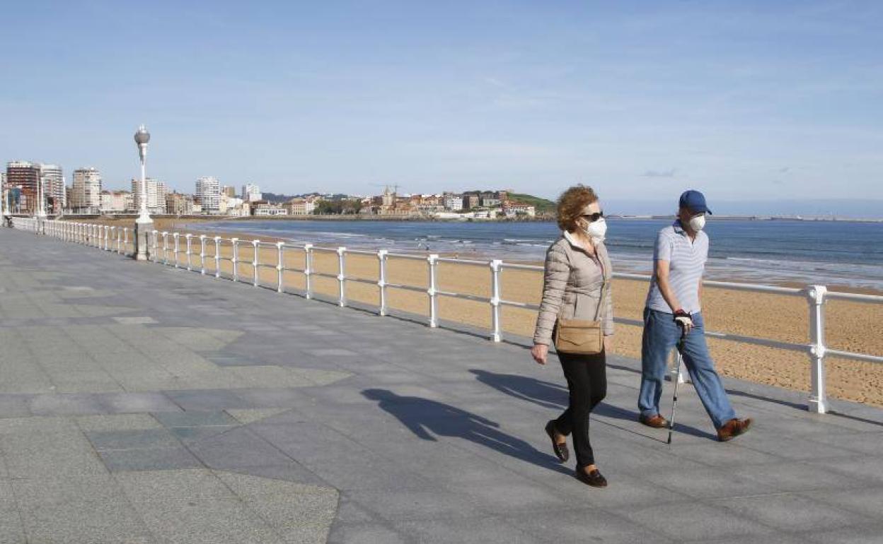 Dos ciudadanos pasean por el Muro de San Lorenzo, en Gijón. 