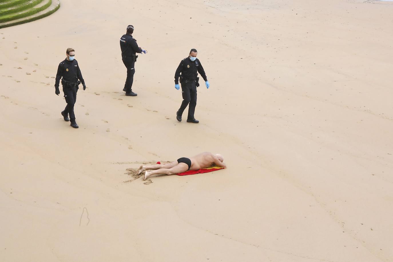 24 de abril. Gijón | Varios agentes de Policía reprenden a un bañista en la playa de San Lorenzo que se saltó el confinamiento. 