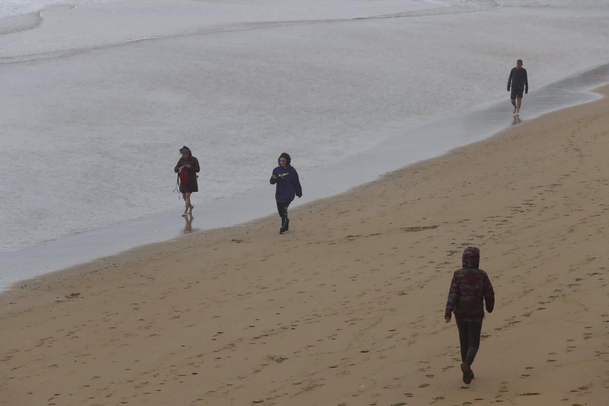 Personas paseando ayer por la arena y la orilla de la playa de San Lorenzo con mal tiempo. 