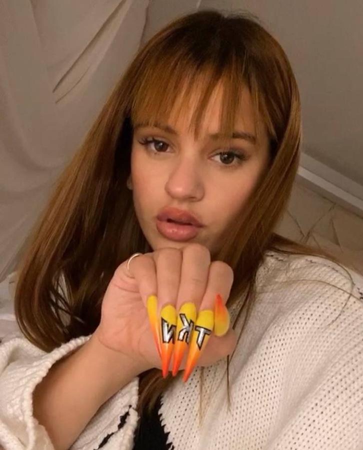 La cantante Rosalía luce siempre algunas de las manicuras más comentadas de la red, como esta que incluye degradado en amarillo y naranja con las siglas TKM y largo XXL como es habitual en ella.