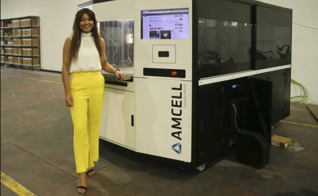 Mariel Díaz posa con una máquina industrial AMCELL de fabricación aditiva de las que fabrica en su nueva nave de Siero.