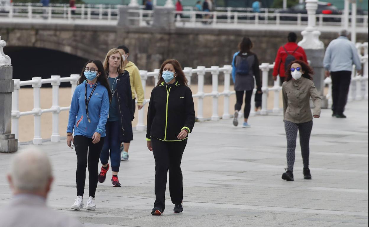 Varias personas pasean por el Muro de San Lorenzo de Gijón.