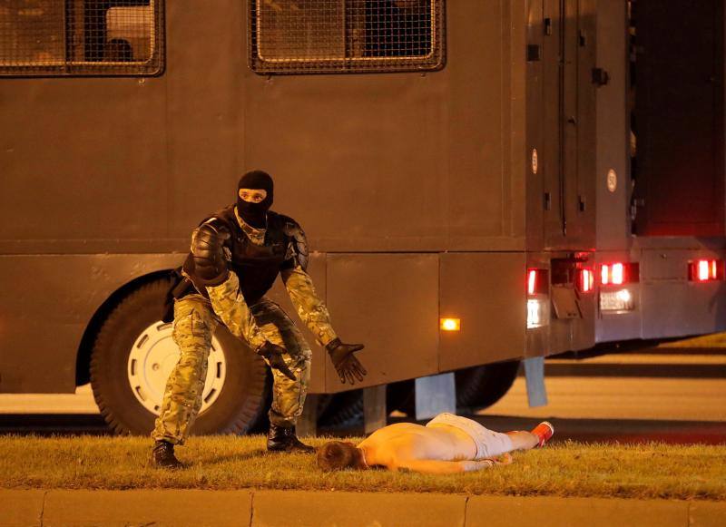 Un agente bielorruso hace un gesto junto a Yevgeny Zaichkin, un manifestante herido, que yace en el suelo tras los enfrentamientos sucedidos después del cierre de las elecciones presidenciales en Minsk, Bielorrusia, el 9 de agosto de 2020. 