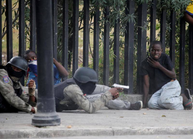 Un niño sentado cerca de un miembro de la Policía Nacional de Haití durante un tiroteo en Champ de Mars, Port-au-Prince, Haití, 23 de febrero de 2020. 