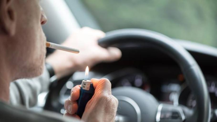 Un hombre enciende un cigarro en su vehículo.