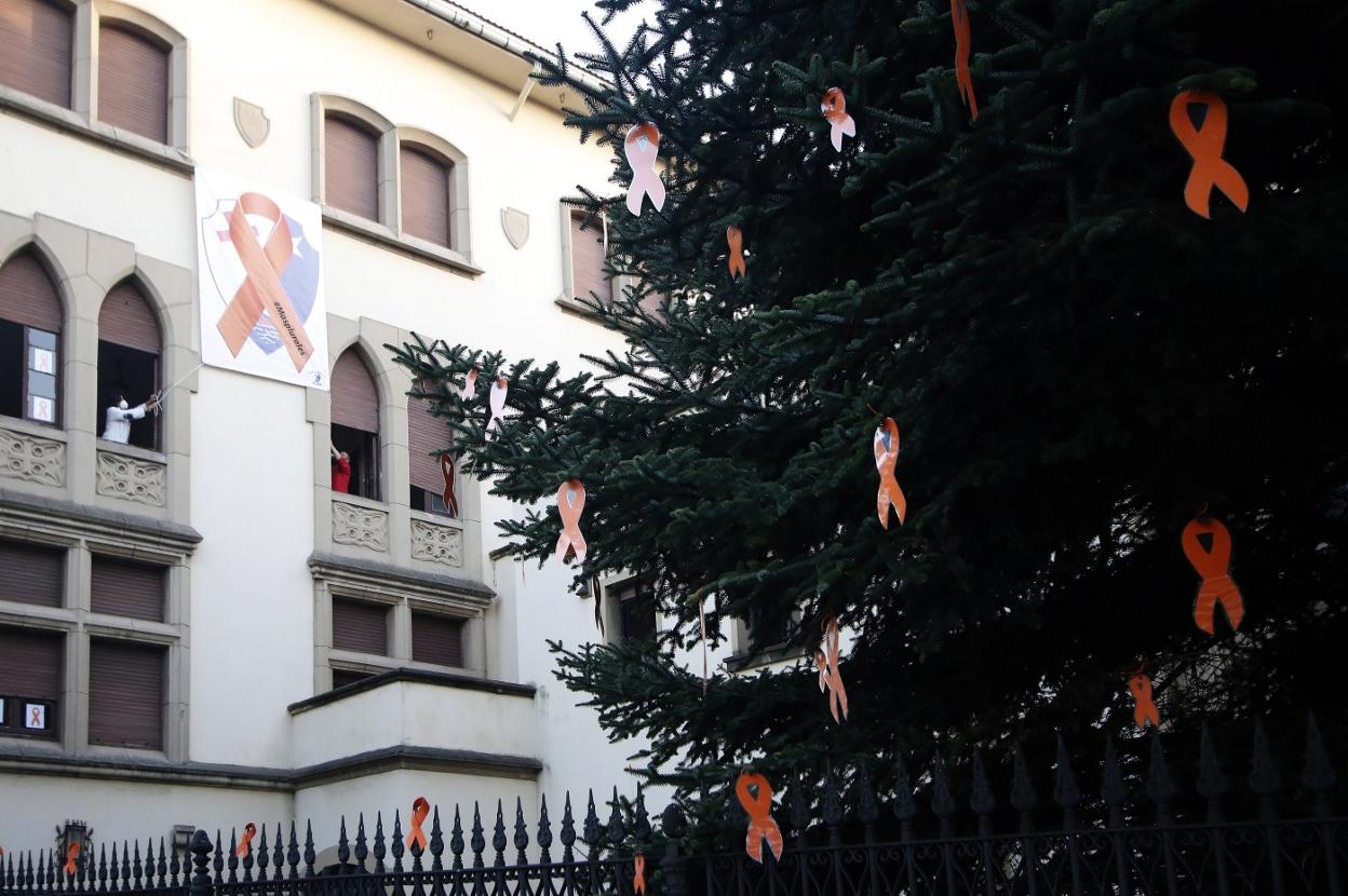 Lazos naranjas colgados en los árboles, la verja y la fachada del Colegio La Asunción de Gijón. 