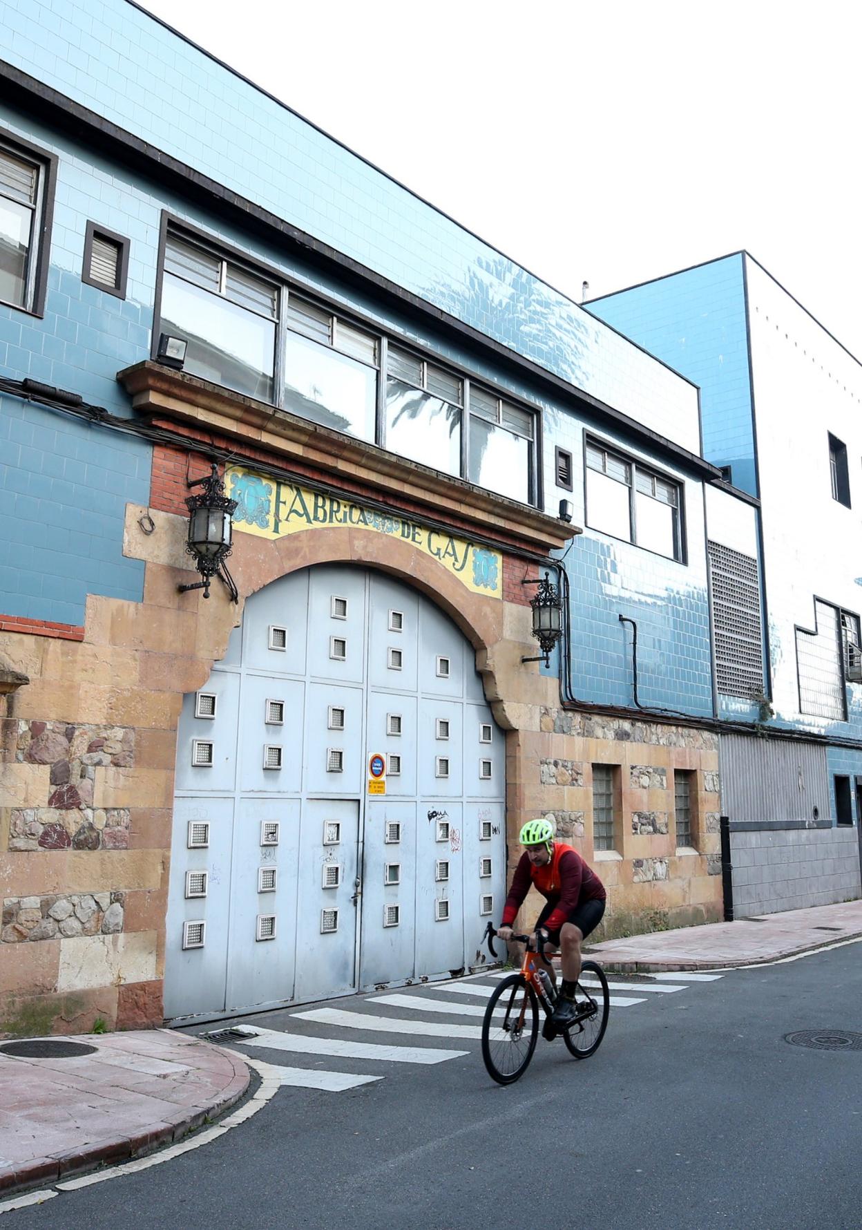 Un ciclista circulando por delante de la fachada principal de la Fábrica de Gas. 