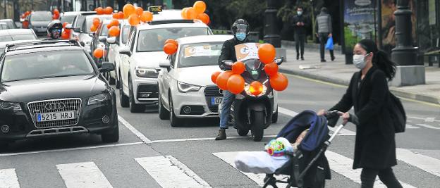 La marcha contra la 'Ley Celaá' pasa por el centro de Oviedo, mientras una vecina cruza por un paso de peatones con su bebé. 