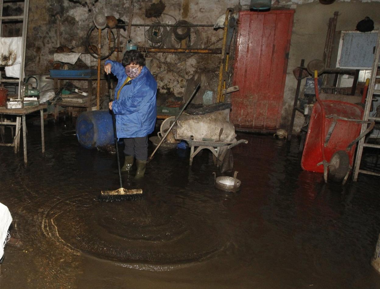 Esperanza Díaz se ayuda de un cepillo para sacar el agua que anega su nave, en Veriña. 