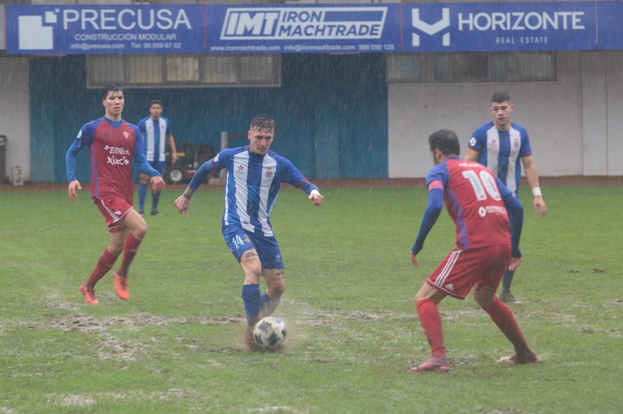 Guille Vázquez golpea el balón en el barrizal con Juan Carlos atento para cortar el pase. 