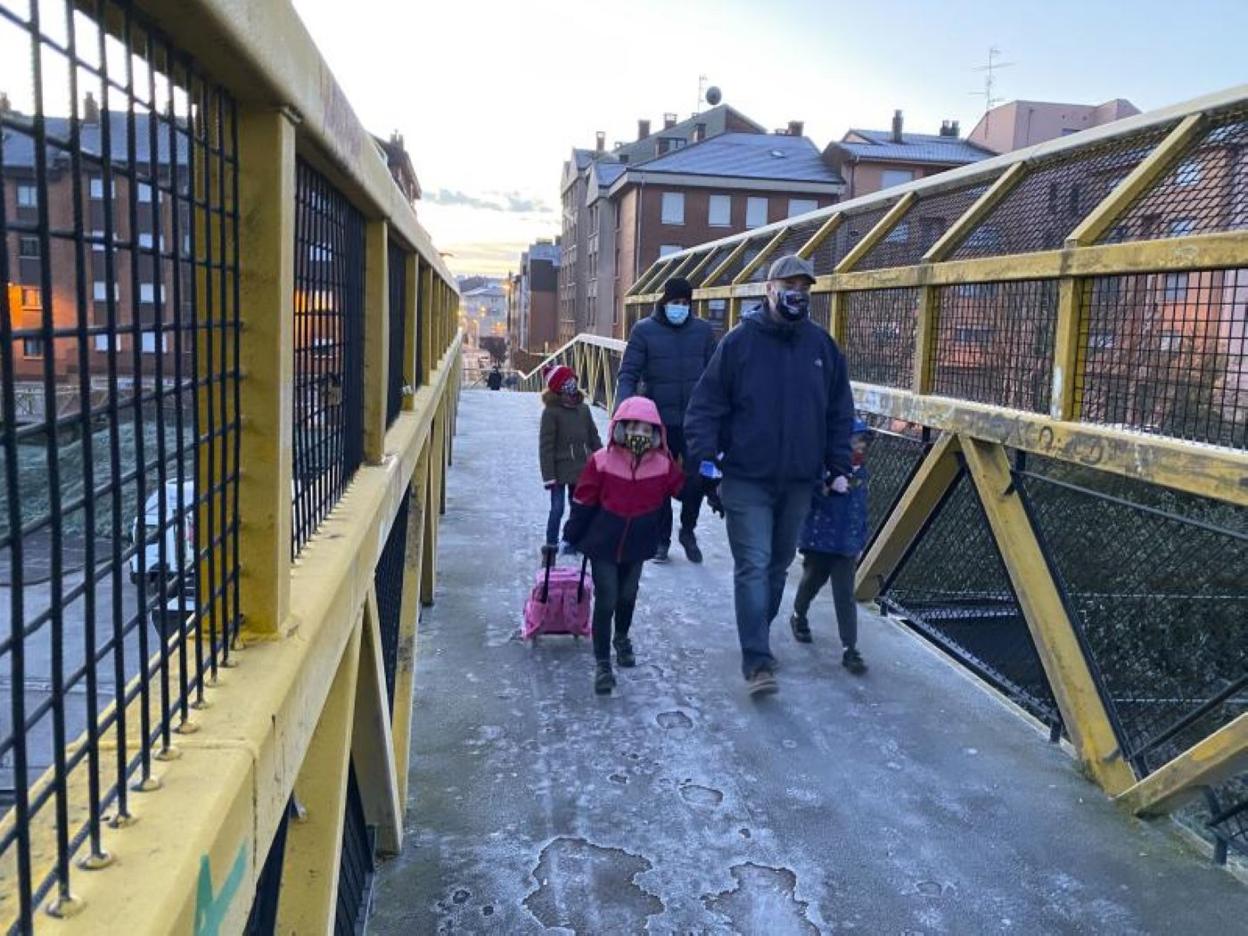 Varias familias cruzan la pasarela de El Carbayu en Lugones para acudir al colegio. 